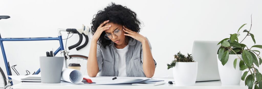 Confused concentrated mixed race woman dressed formally wearing big round eyeglasses being focused on her future project having some problems with it. Serious woman being busy at her workplace